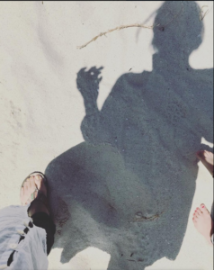 白い砂浜を歩く女性の影