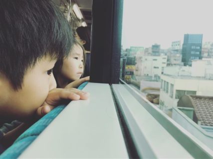 電車の中から窓の外を眺める少女と少年
