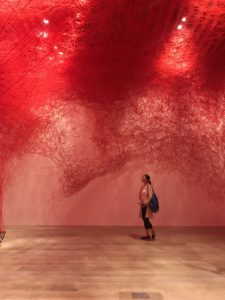 塩田千春展魂がふるえるの赤い糸が張り巡らされた展示を眺める女性